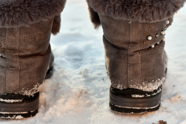 棕色毛茸茸的女人的冬天靴子在雪地上的特写。图片下载