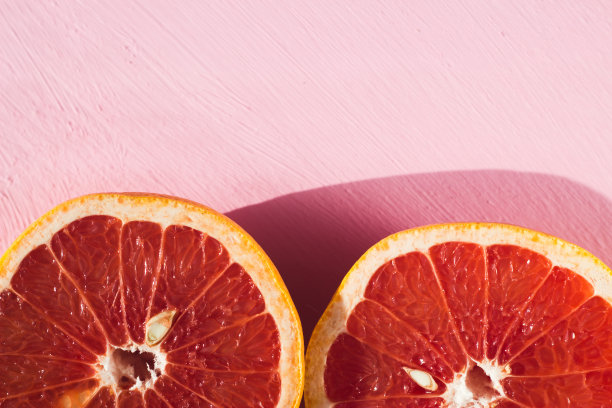 一半的红柑橘在粉红色的背景下在阳光下。图片下载
