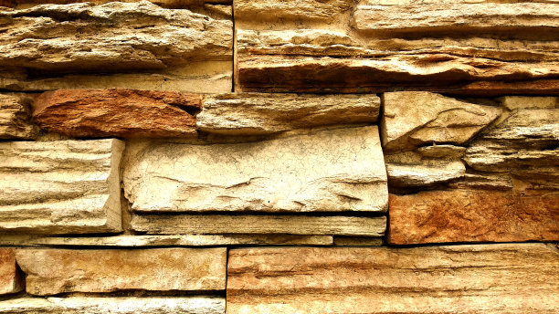 石头墙,特写。传统的石墙由不同大小的矩形石头制成，颜色为明亮的沙子和橙色。中世纪的石墙图案。背景图片下载