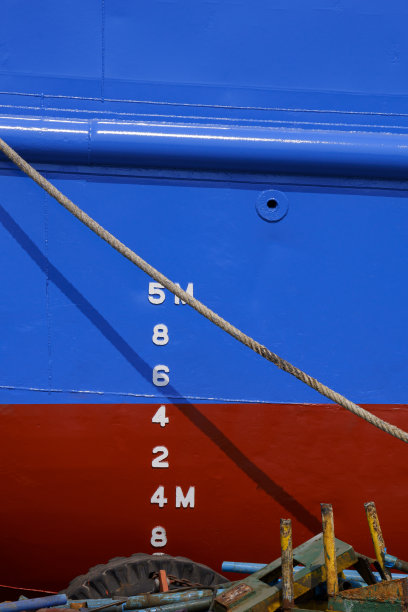 船坞蓝色和红色防锈船体上的吃水标志编号，系泊绳和生锈的金属废料堆图片下载