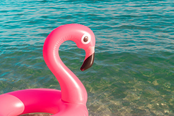 粉红色的池。粉红色的充气火烈鸟在蓝色的海水在夏季海洋海滩的背景。池浮动。图片下载