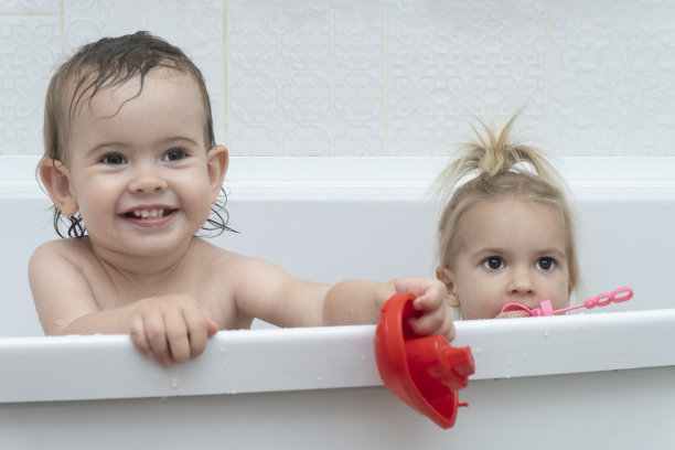 肖像的两个小高加索可爱的女孩姐妹坐在浴缸，有时间洗澡，玩洗澡玩具，微笑，白色的背景，复制空间。图片下载