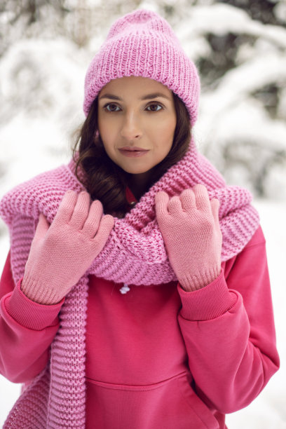 一个穿着粉红色衣服，夹克，针织围巾和帽子的女人站在雪地里的森林里图片下载