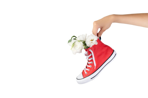 女人的手拿着时髦的红色球鞋与鲜花图片下载