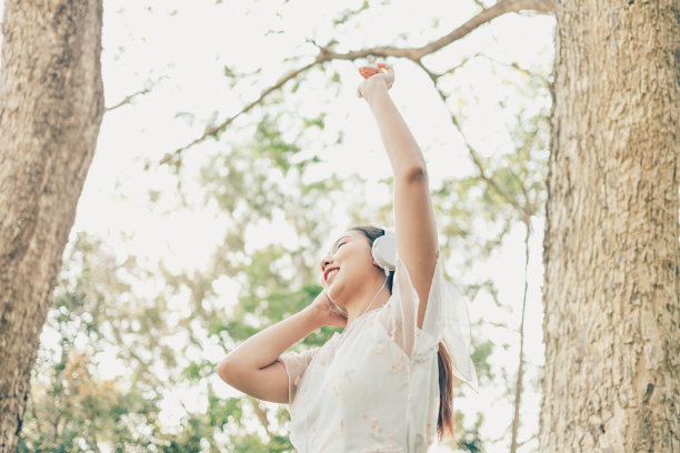 一个戴着耳机的女孩在森林里听着音乐跳舞。音乐爱好和野餐概念。图片下载