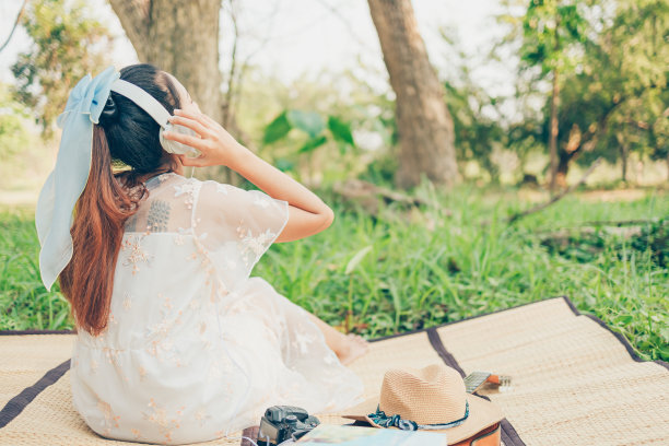 一个戴着耳机的女孩在森林里听着音乐跳舞。音乐爱好和野餐概念。图片下载