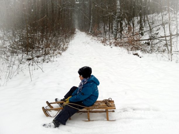 快乐的小男孩在雪地里拉着雪橇图片下载