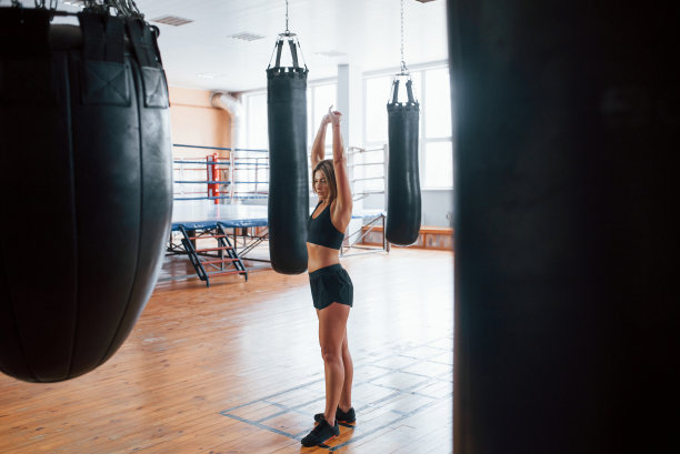 完整的照片。健身房黑色沙袋旁的女人，自然采光图片下载