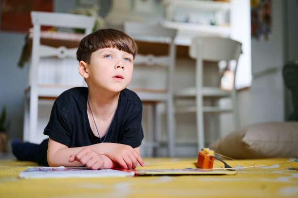 一个学前班的白人男孩躺在家里的地板上，看书看图片。家庭教育的概念图片下载