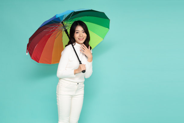 年轻快乐的亚洲女人拿着五颜六色的伞孤立在绿色的背景图片下载