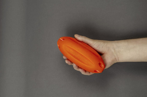 手持橙色橡胶球在灰色背景。图片下载