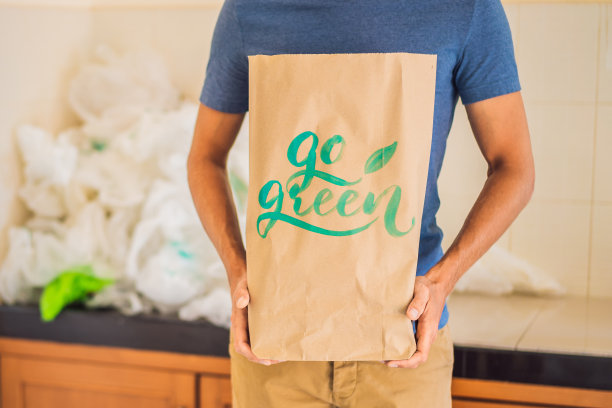 一名男子在一堆塑料袋中拿着一个写有“GO GREEN”字样的包裹。“零浪费”的概念。世界环境日的概念图片下载