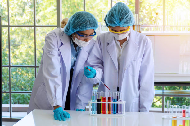 一组化学人员在实验室工作。两个年轻的亚洲女性研究科学家穿着实验室外套，手套和眼镜分析实验一起在实验室，看试管。科学的概念。图片下载