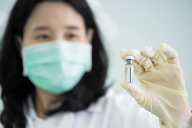 科学家戴着医用口罩和白大褂，手里拿着新冠疫苗小瓶。医生看着瓶子，成功研制出了冠状病毒疫苗。选择性聚焦在小瓶上图片下载