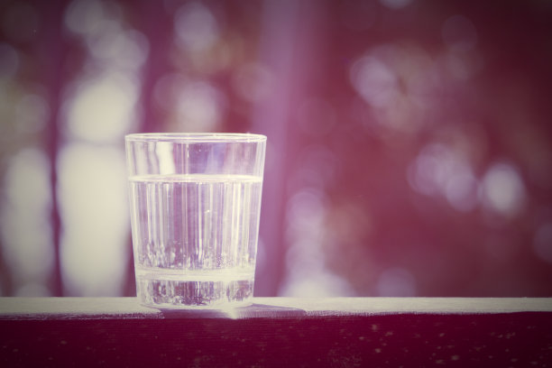 水杯放在阳光下的木板上。水合在炎热的夏天概念。健康的生活方式的象征。健康水饮料色调紫色图片下载