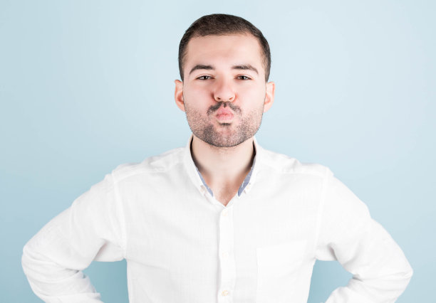 有趣的人，他的嘴唇，好像要亲吻某人，期待着，孤立在一个蓝色的背景。时髦的大胡子男人表达积极的情绪，做鬼脸图片下载