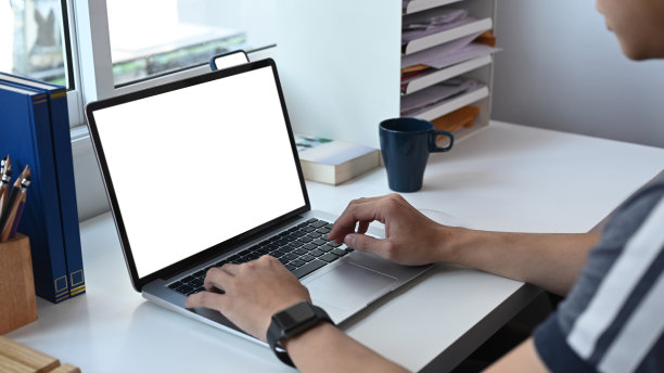 一名年轻人坐在家里的办公室里用笔记本电脑搜索互联网上的信息。图片下载