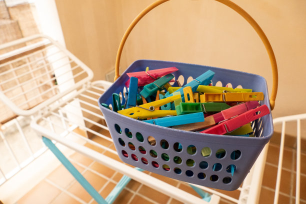 篮子里放着彩色的晒衣夹，后面放着白色的晾衣架图片下载