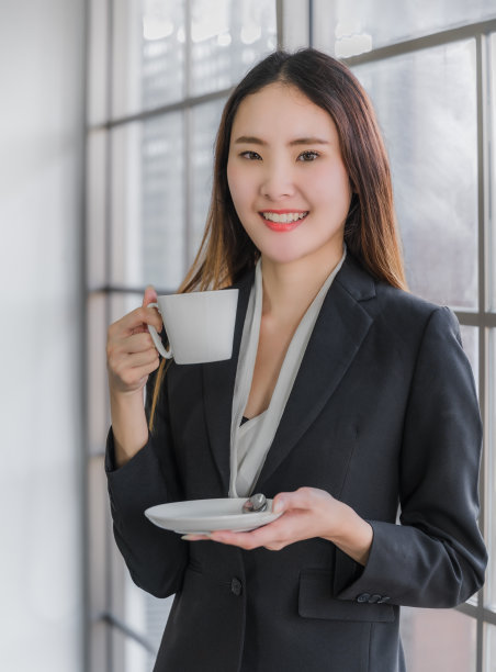 美丽的年轻亚洲女商人穿着西装，手拿白色咖啡杯图片下载