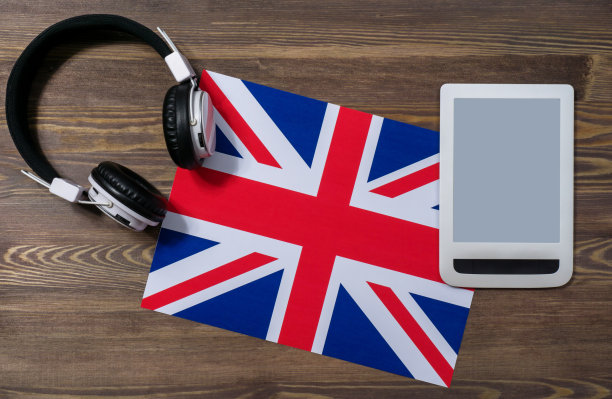 英国国旗上放着电子耳机和白色平板电脑。特写，棕色木制背景，俯视图。在线英语课程。Moskup广告图片下载