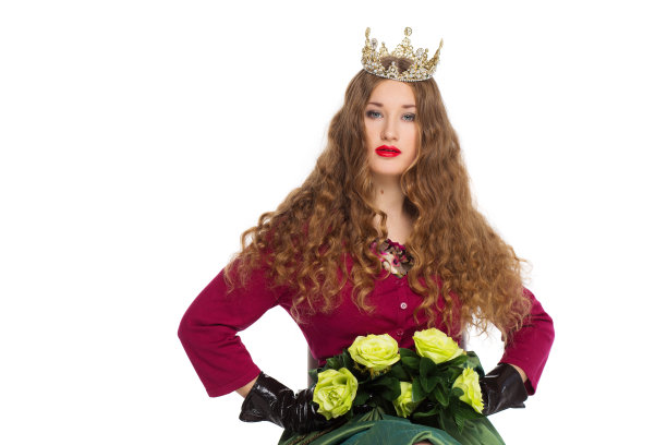 美丽优雅的年轻少女与长卷曲的头发在皇冠和一个相当长的绿色长裙孤立在白色的背景。图片下载