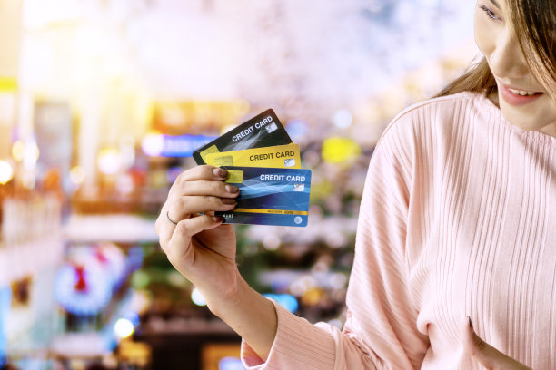 手的年轻女子显示为支付购物中心的背景。快乐的女孩拿着卡片在她的手在模糊的百货商店背景。货币交易和购物概念。图片下载