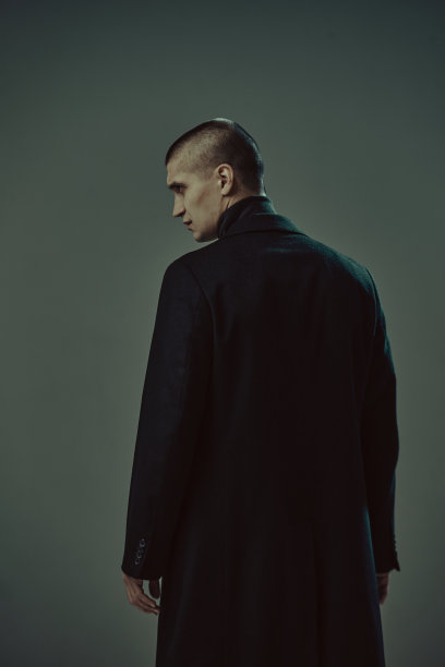 勇敢的短发男子穿着黑色大衣侦探或罪犯在灰色演播室背景，背景图片下载