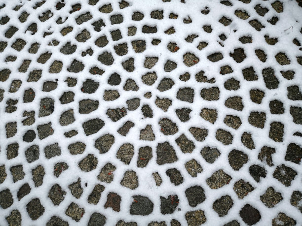 由积雪形成的几何圆形雪图案覆盖着路面鹅卵石的轮廓。自然与工艺制作的灰白色原始径向对称圆形图案图片下载