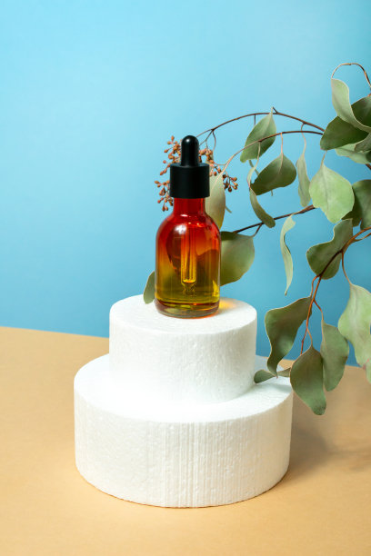 抗衰老面部精华液与吸管玻璃瓶在蓝色和米色背景。讲台上的化妆品精油图片下载