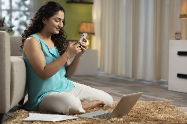 一张年轻女子坐在家里地板上用手机的照片，库存照片图片下载