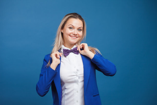 蓝色背景上穿着蓝色衣服的快乐微笑的年轻女子。友好的商业肖像图片下载