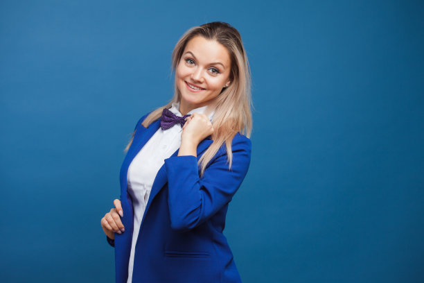 穿着蓝色夹克和紫色领结的滑稽商务女士。工作室肖像在蓝色背景图片下载