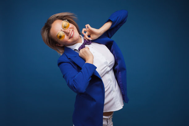 穿着时髦的蓝色夹克，打着领结的女商人跳来跳去。一个快乐的女孩的肖像图片下载
