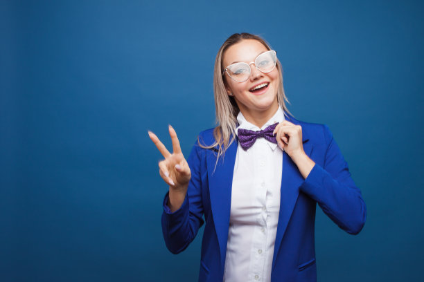 穿着蓝色夹克和紫色领结的滑稽商务女士。高兴得跳起来，竖起两个大拇指表示胜利。图片下载