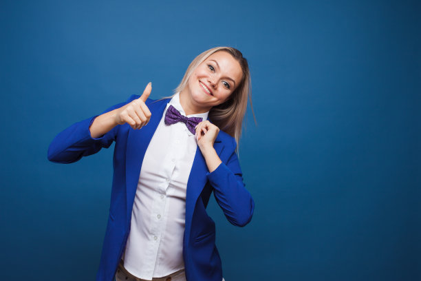 穿着蓝色夹克和紫色领结的滑稽商务女士。高兴得跳起来，竖起大拇指。图片下载