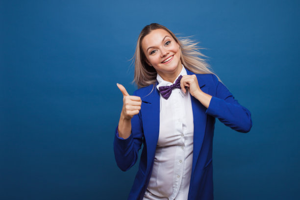 穿着蓝色夹克和紫色领结的滑稽商务女士。高兴得跳起来，竖起大拇指。图片下载