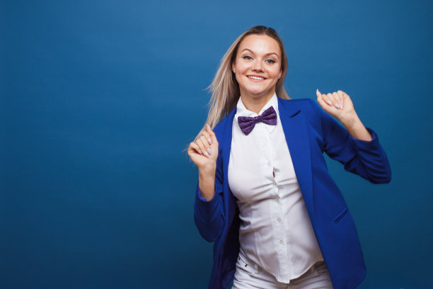 穿着时髦的蓝色夹克，打着领结的女商人跳来跳去。一个快乐的女孩的肖像图片下载