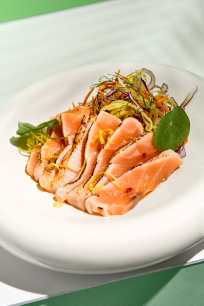 芝麻三文鱼tataki配沙拉。鱼生鱼片餐厅的开胃菜，白色的桌子与绿色的墙壁。白天的阳光和热带棕榈叶的阴影。夏季或春季的食物概念。图片下载