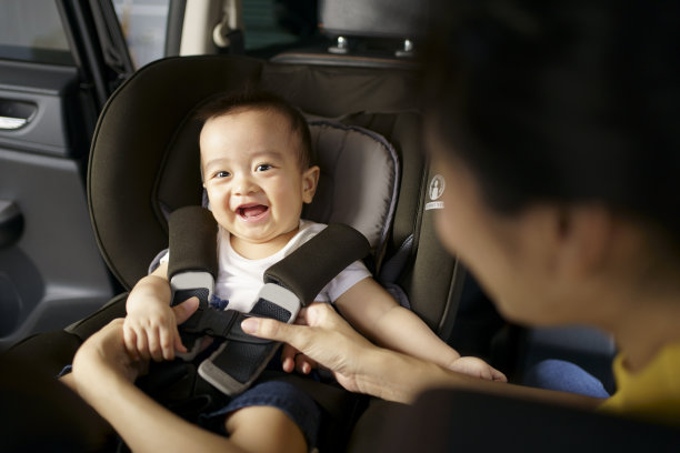 亚洲小宝宝在汽车安全座椅上系好安全带时快乐玩耍。一个男孩看着他的母亲并在车里微笑图片下载