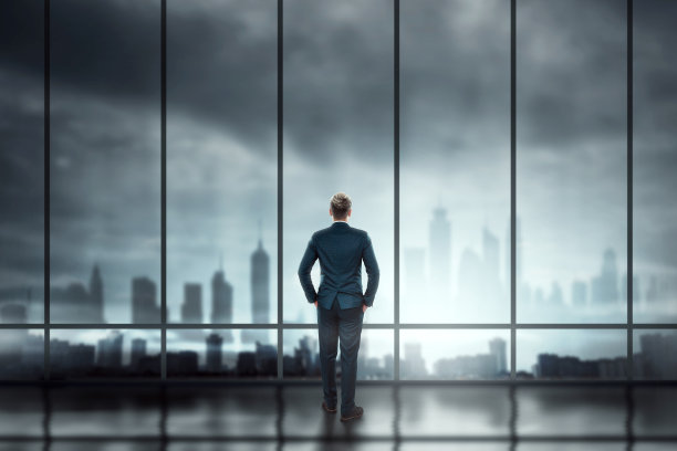 穿着商务西装的商人站在大窗户前眺望城市图片下载