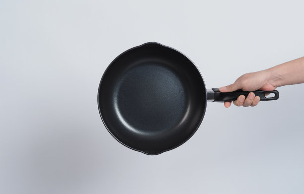 清洁锅底，身着灰色T恤的男士用方便的洗碗海绵擦拭不粘锅，软面泛黄，硬面泛绿，便于烹饪后的卫生。白色背景。图片下载