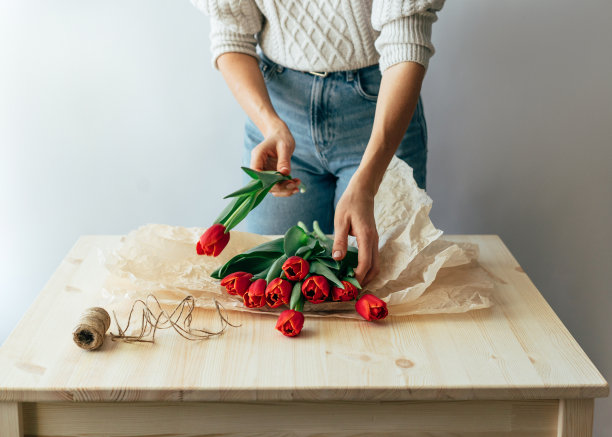 一个穿着毛衣的陌生女人正在打包一束红色郁金香。图片下载