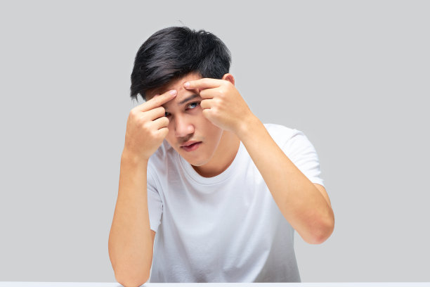 一位年轻英俊的亚洲男子挤了挤额头上的青春痘。图片下载