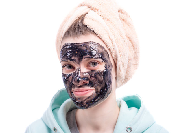 年轻迷人的女人与毛巾在她的头和一个保湿面膜在她的脸近距离在一个白色的背景，复制空间图片下载