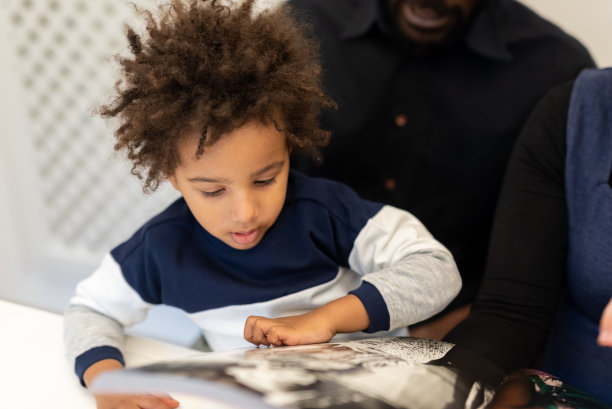 温柔的混血孩子在父亲的怀抱中为孩子们读童话故事，孩子翻阅书页时惊讶的表情的细节，父母家庭教育的概念图片下载