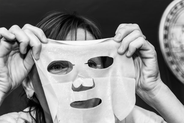 一名年轻女子在脸上敷了一个白色保湿面膜，黑白照片图片下载