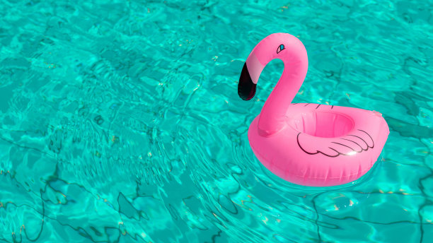 海滩火烈鸟。粉红色的充气火烈鸟在游泳池的水为夏天的海滩背景。时尚的夏天的概念。图片下载