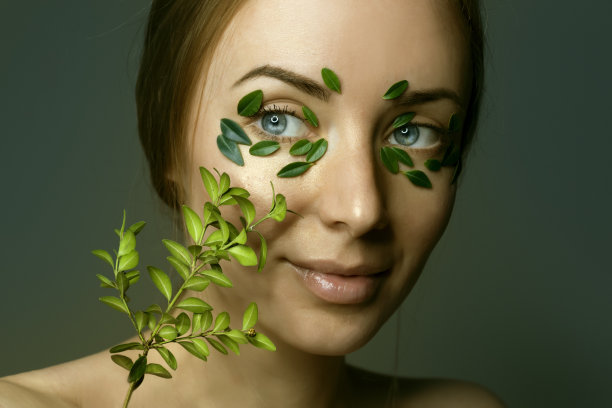 年轻女子肖像与自然化妆模糊与散焦黄杨木枝。绿叶贴在脸上。草药的概念。图片下载