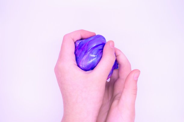 在白色的背景上，有人手中有两种颜色的蓝色和粉红色黏液的游戏的特写。粘液被手压碎、拉伸、撕裂和挤压图片下载
