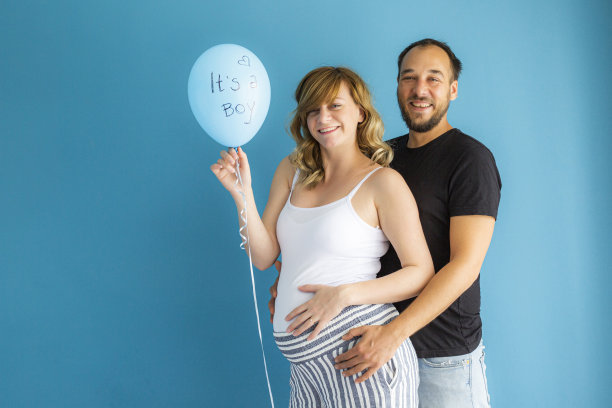 年轻夫妇与“是个男孩”气球在蓝色墙壁前图片下载